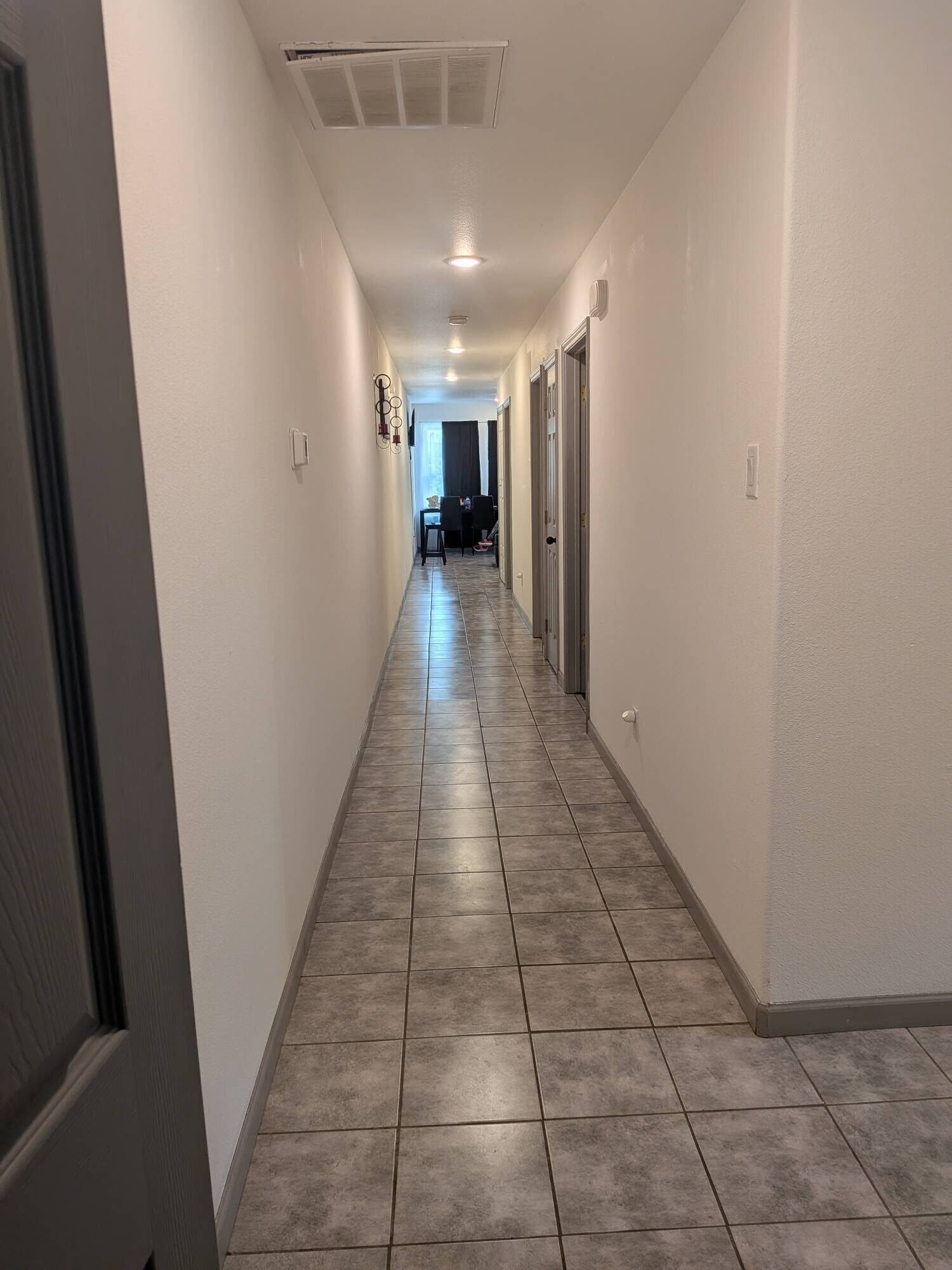 Un pasillo con piso de baldosas, paredes blancas y una puerta al final.