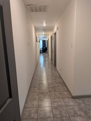 A hallway with tiled flooring, white walls, and a door at the end.
