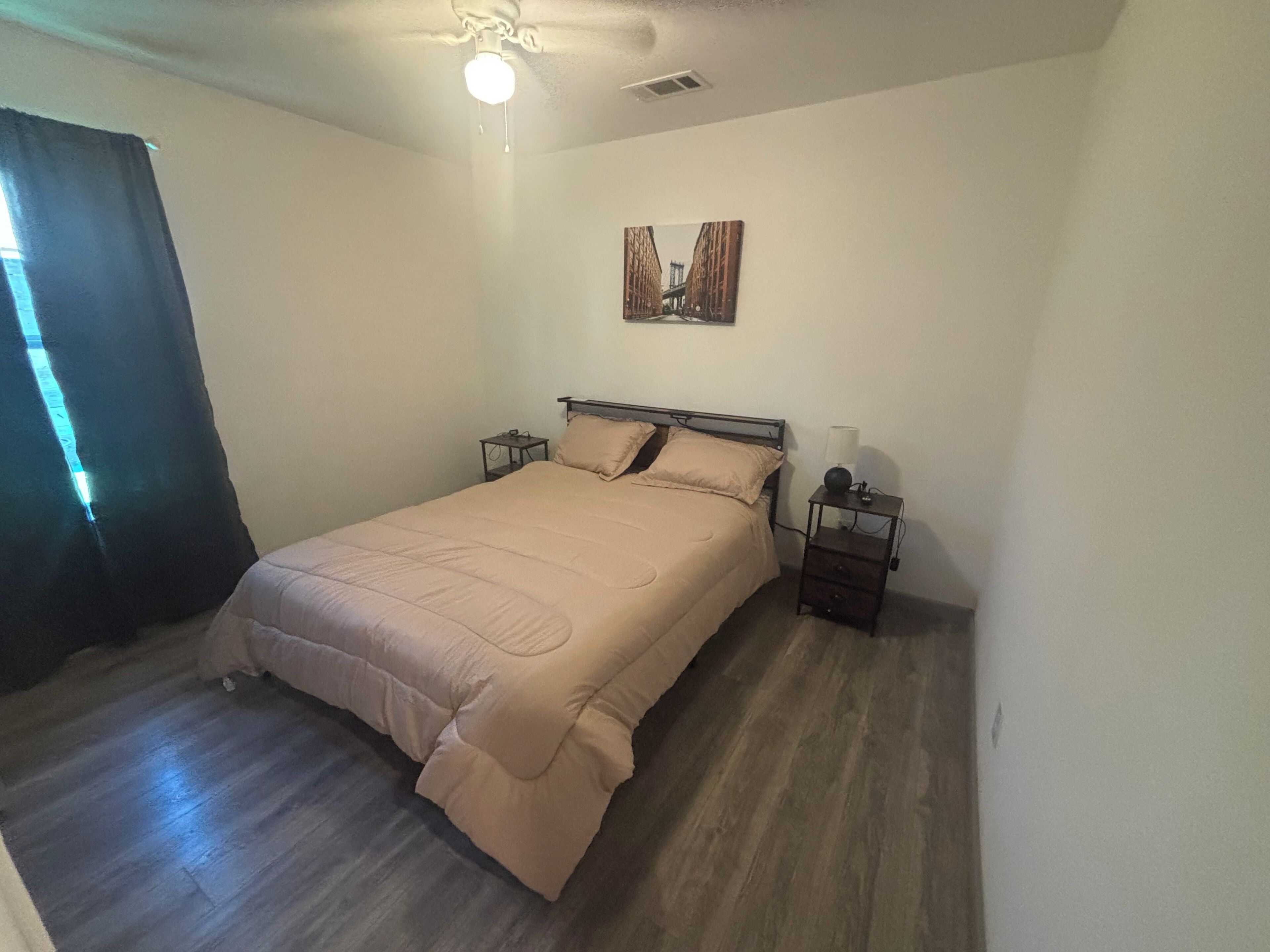 Een slaapkamer met een bed, nachtkastjes, een plafondventilator en een schilderij aan de muur.