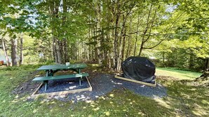 Un tavolo da picnic e una griglia coperta in una zona boschiva.