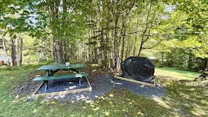 Ein Picknicktisch und ein überdachter Grill in einer bewaldeten Gegend.