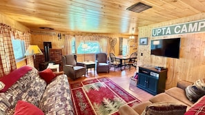 Ein gemütliches Blockhaus-Interieur mit Kamin, Fernseher, Essbereich und einem Schild mit der Aufschrift 'UPTA CAMP'.