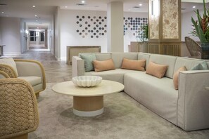 Een moderne woonkamer met een hoekbank, een ronde salontafel en een decoratieve wand met ronde patronen.
