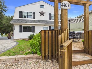 A modern building with a star on the facade, a wooden gate with a number sign, and a patio area with outdoor furniture.