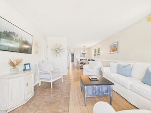 A spacious living room with a white sofa, a coffee table, and a white armchair.