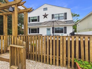 A white building with a star on the facade, a wooden fence, and a pergola with a light fixture.