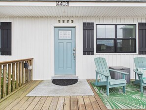 A house with a light blue door, a number '4403' above it, and a porch with two green chairs and a small table.