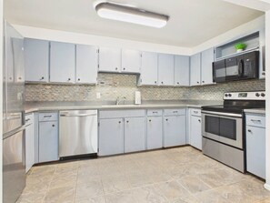 A modern kitchen with grey cabinets, a stainless steel dishwasher, a double oven, and a microwave.