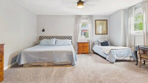 Un dormitorio con cama, mesita de noche, silla, escritorio y ventilador de techo.