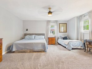 Ein Schlafzimmer mit einem Bett, einem Nachttisch, einem Sessel, einem Schreibtisch und einem Deckenventilator.