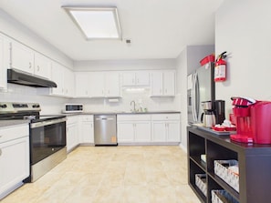 A modern kitchen with white cabinets, stainless steel appliances, and a tiled floor. - `The Kelly` - The Cottage Collection (Virginia Beach)