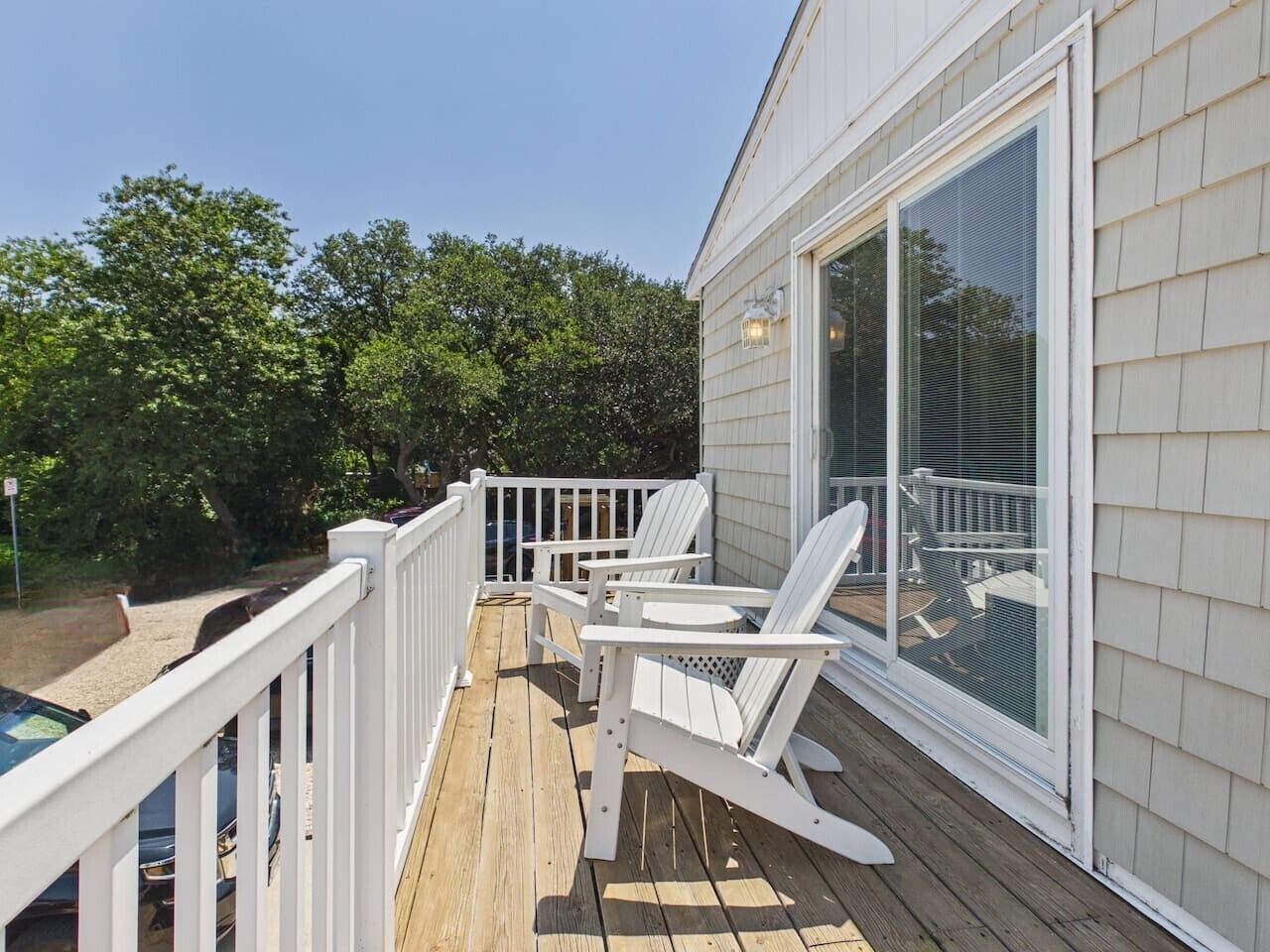 A wooden deck with white railings and two Adirondack chairs.