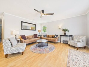 Ein Wohnzimmer mit einer Sofagarnitur, einem Couchtisch, einem gemusterten Teppich, einem Deckenventilator und einem Beistelltisch mit einer Lampe.