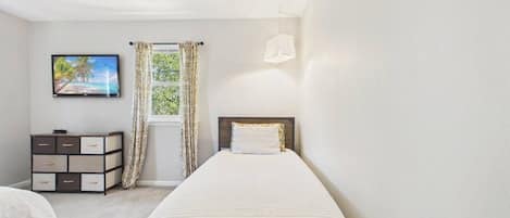 A bedroom with a bed, a TV, a dresser, and a window with curtains.