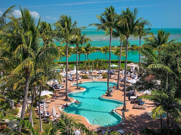 Een zwembadcomplex van een resort met meerdere zwembaden, omgeven door palmbomen en ligbedden.