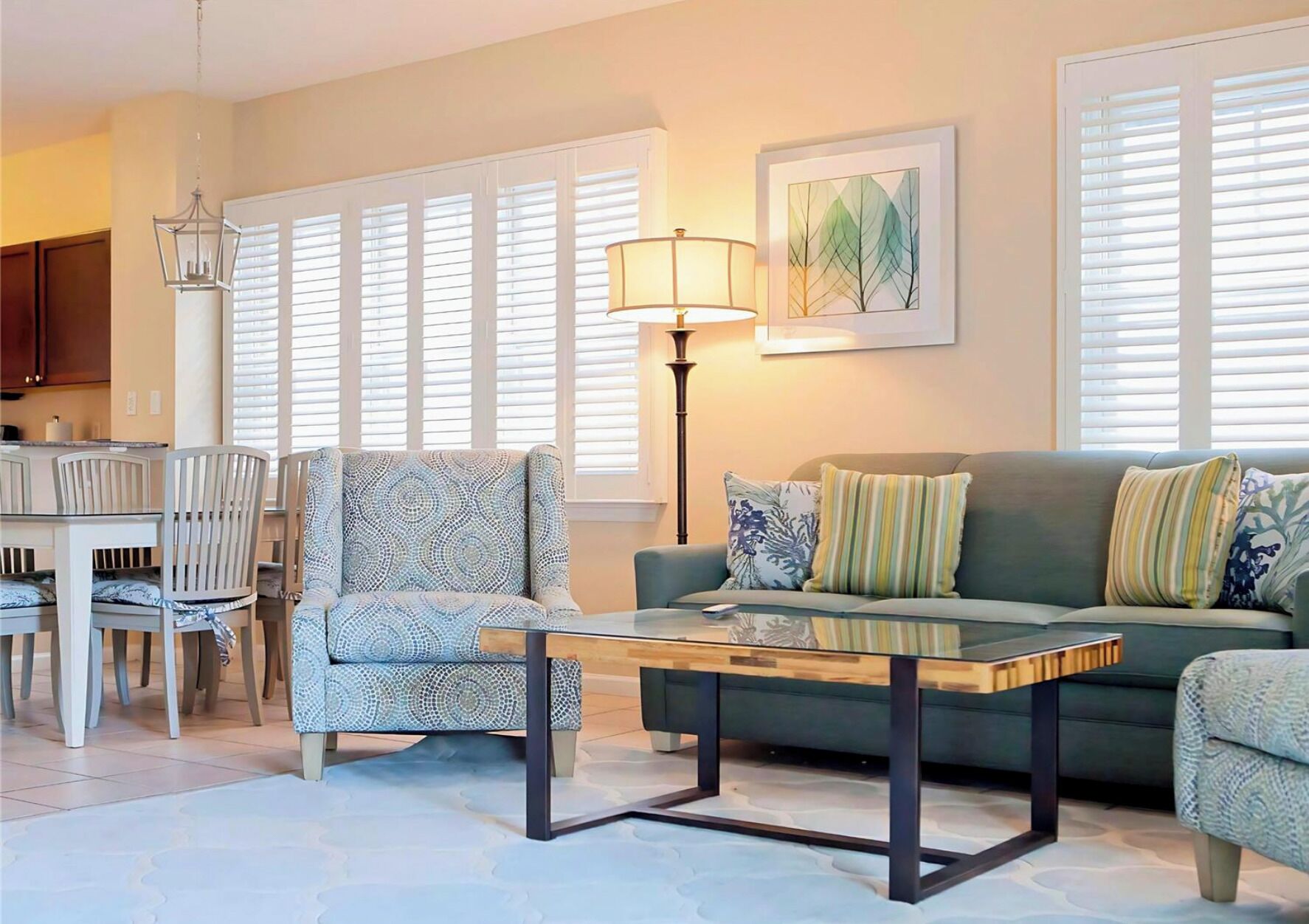A living room with a sofa, armchair, coffee table, dining table, chairs, and a lamp.