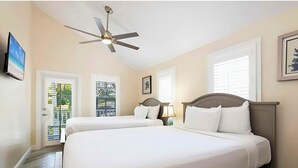 Une chambre d’hôtel avec deux lits, un ventilateur de plafond, une télévision et une fenêtre avec des stores.