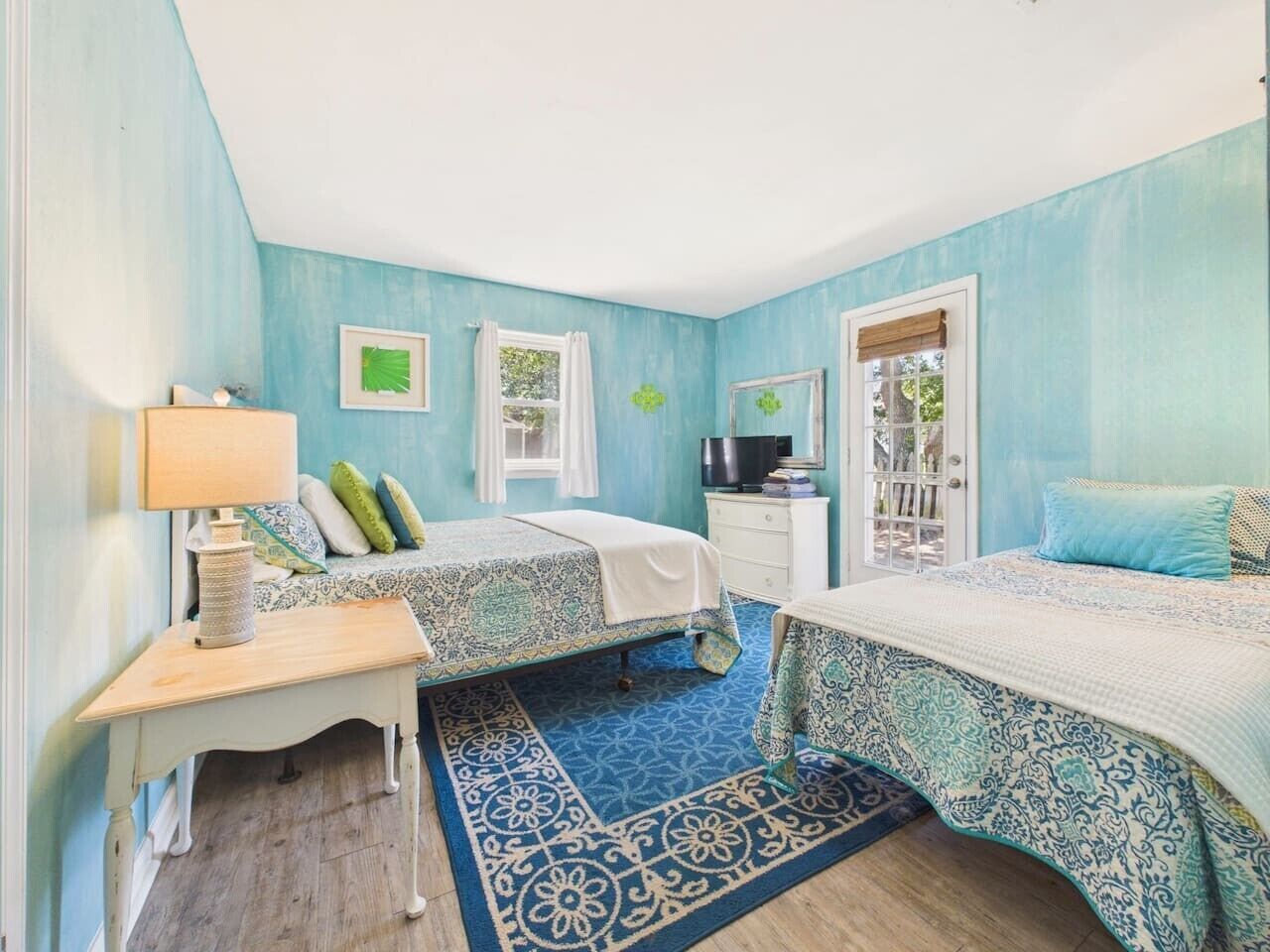 A bedroom with two beds, a desk, a chair, a TV, and a window with curtains.