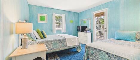 A bedroom with two beds, a desk, a chair, a TV, and a window with curtains.