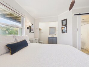 Quarto com uma cama grande, mesa de cabeceira, espelho e janela.