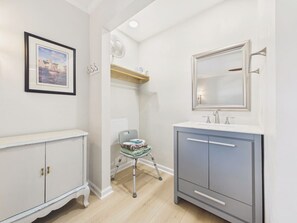 A bathroom with a vanity, a mirror, a framed picture on the wall, and a chair. - `The Greyson` - The Cottage Collection (Virginia Beach)