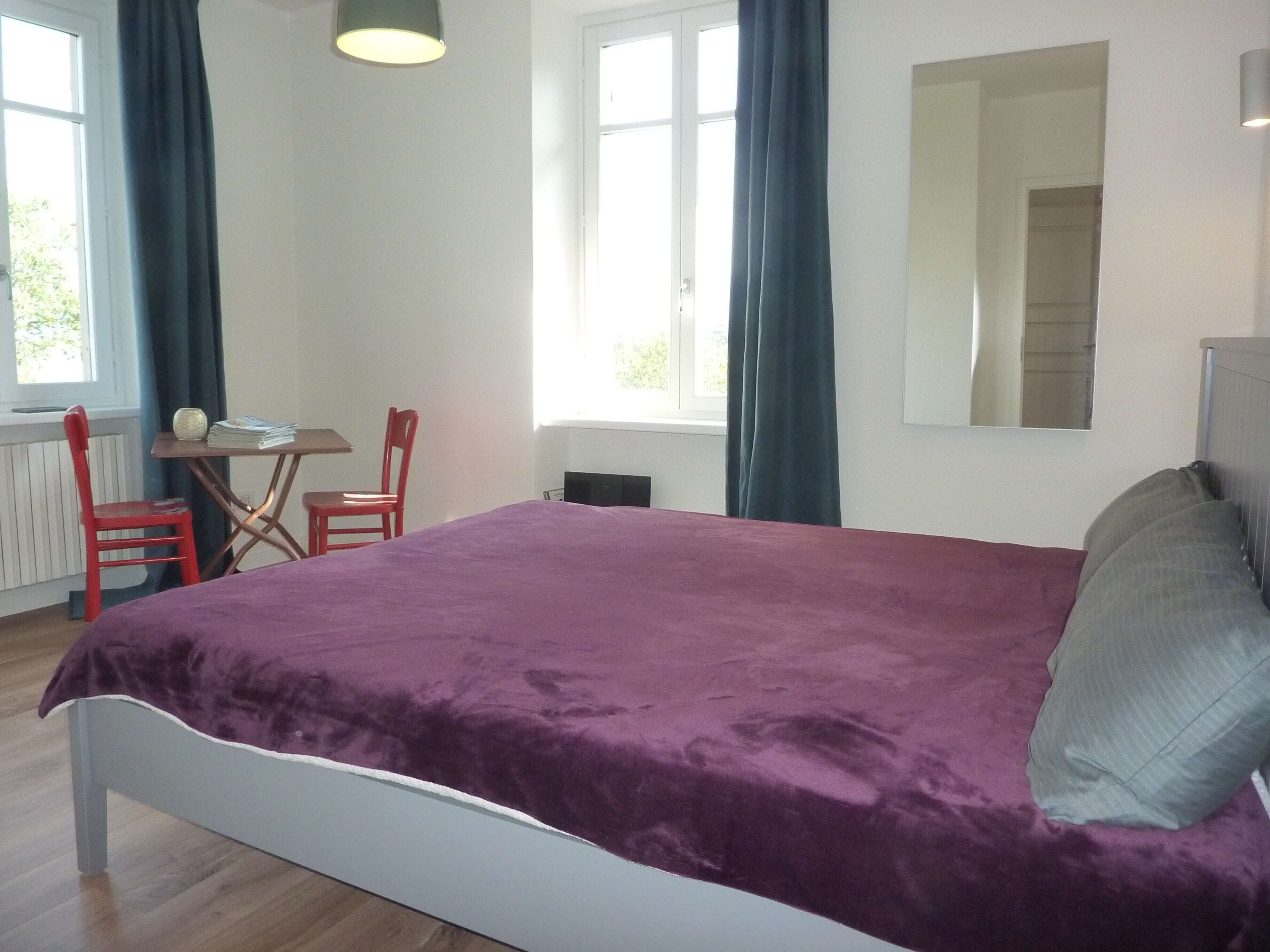 A bedroom with a bed, a desk, a chair, and a window with curtains.