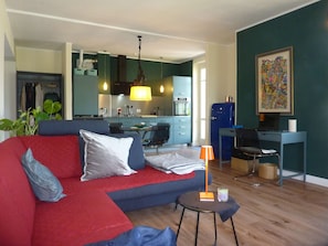 Ein Wohnzimmer mit einer Couch, einem kleinen Tisch, einer Lampe und einer Küche im Hintergrund.