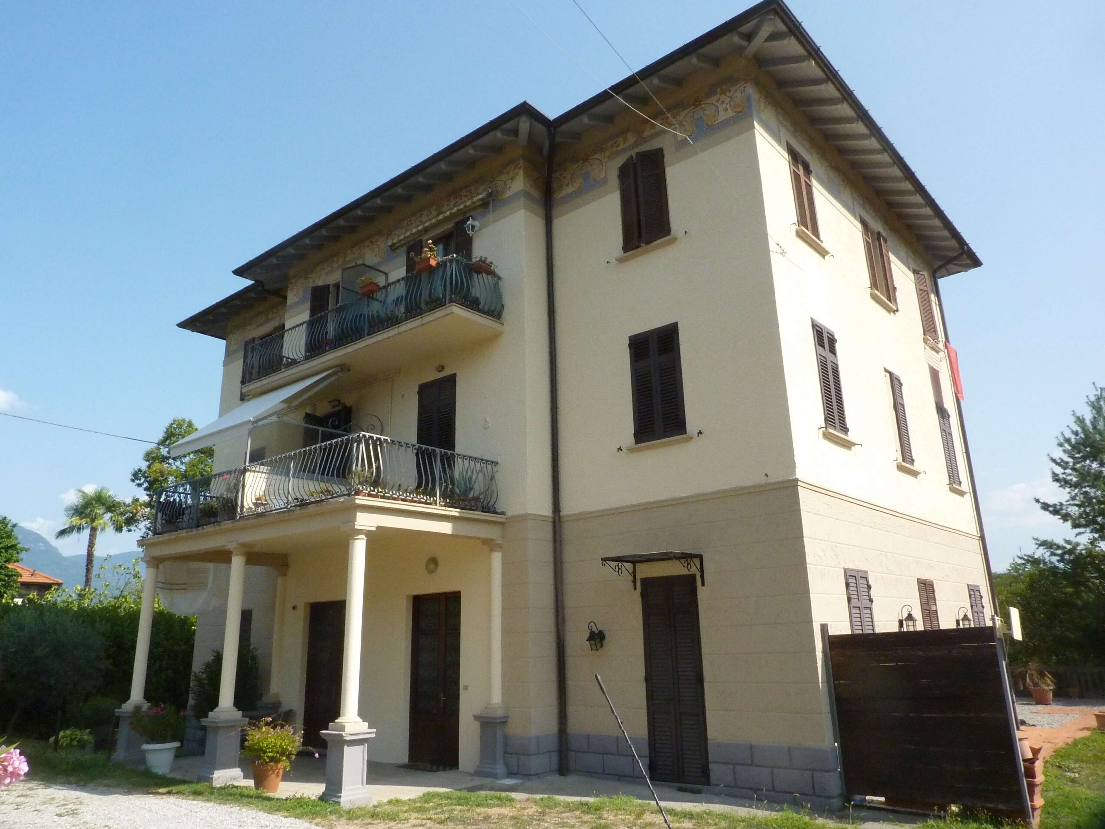 A two-story building with a balcony, a covered entrance, and a garden area.