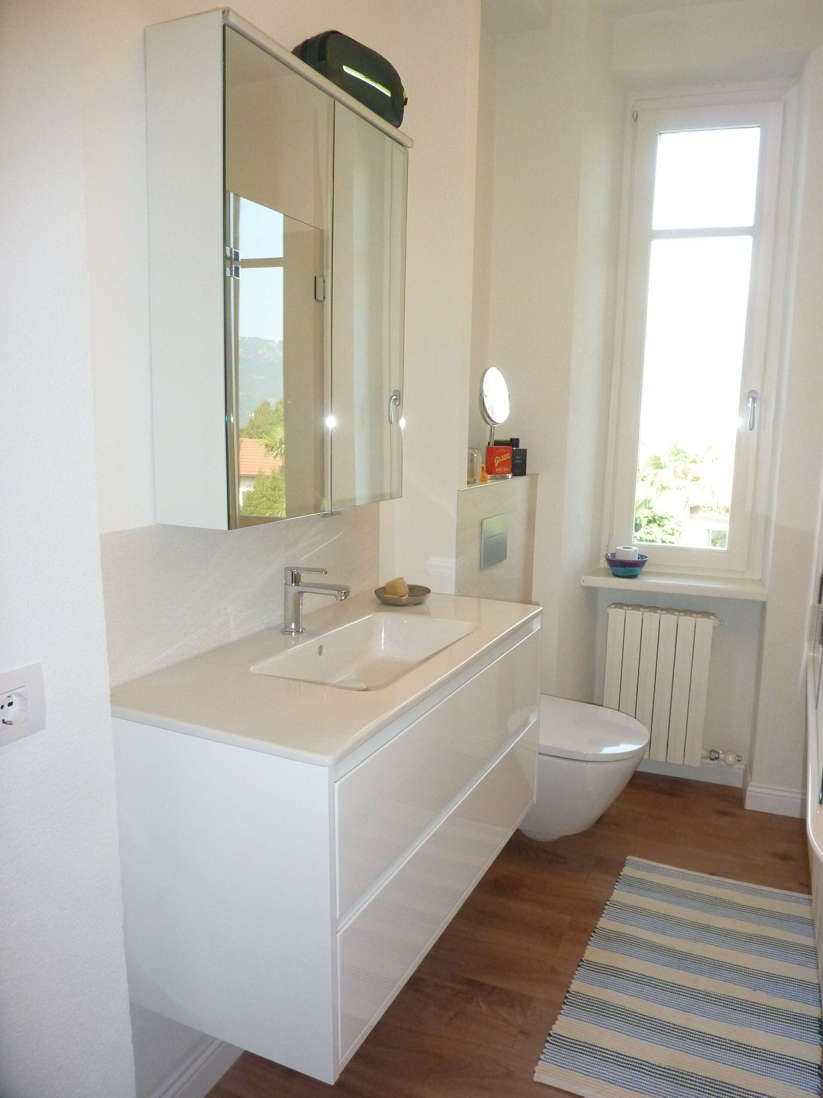 A bathroom with a white sink, mirror, and toilet. There is a window with a view of greenery outside.