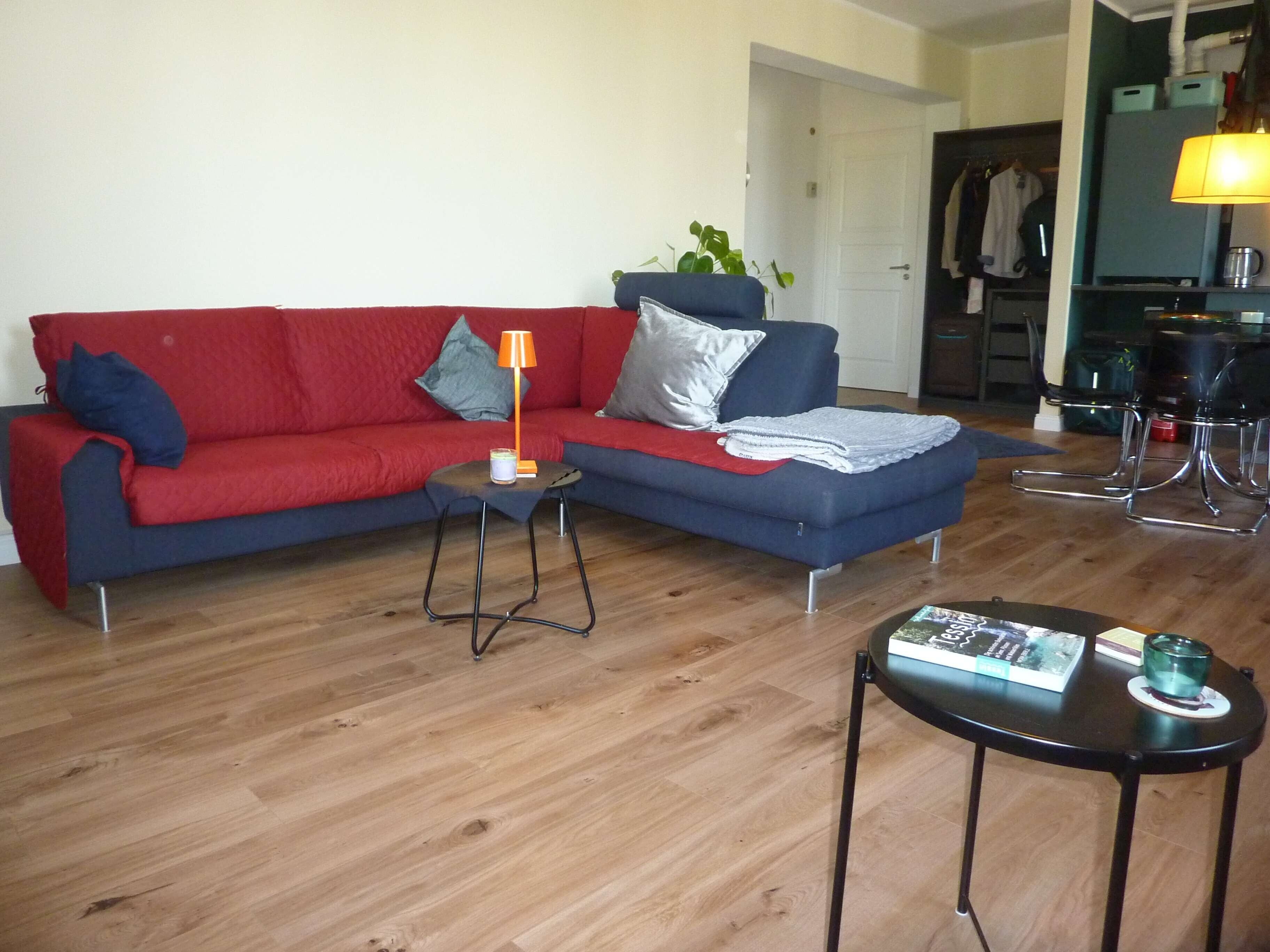 Ein Wohnzimmer mit einem roten Sofa, einem kleinen Beistelltisch, einer Lampe und einem Couchtisch.