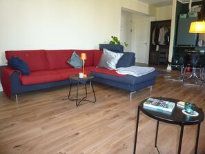 Una sala de estar con un sofá rojo, una mesita auxiliar, una lámpara y una mesa de centro.