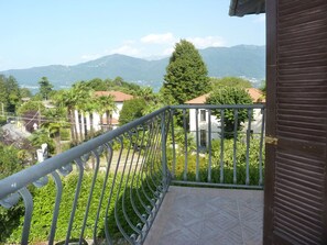 Ein Balkon mit Metallgeländer, der auf ein Wohngebiet mit Häusern und Grünflächen sowie entfernte Berge blickt.
