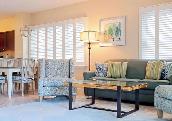 A living room with a sofa, armchair, coffee table, dining table, chairs, and a lamp.