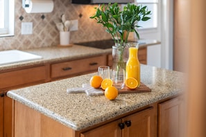 Un comptoir de cuisine avec un verre de jus d’orange, une planche à découper avec des oranges et un vase contenant des plantes vertes.