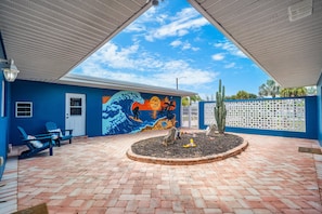 A covered outdoor area with a blue wall featuring a mural, a circular garden bed, and a white fence. - Family‑Friendly Tropical Beach Home w/ Private Pool ☀️ (Indian Harbour Beach)