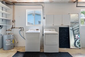 Une buanderie équipée de deux machines à laver et deux sèche-linge, d’un chauffe-eau et d’une fenêtre donnant sur un immeuble.