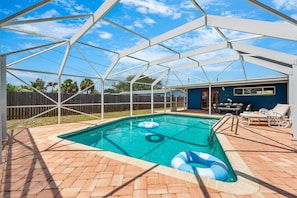 Une piscine extérieure couverte, avec une terrasse en briques, des chaises longues et une clôture en bois en arrière-plan.