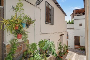 A narrow street with buildings on either side, some with balconies and potted plants.