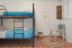 A dormitory room with bunk beds, a small table with a Buddha statue, and a patterned rug.