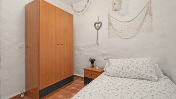 Un dormitorio con un armario de madera, una mesita de noche con un florero y un objeto decorativo, y una cama con edredón estampado de flores.
