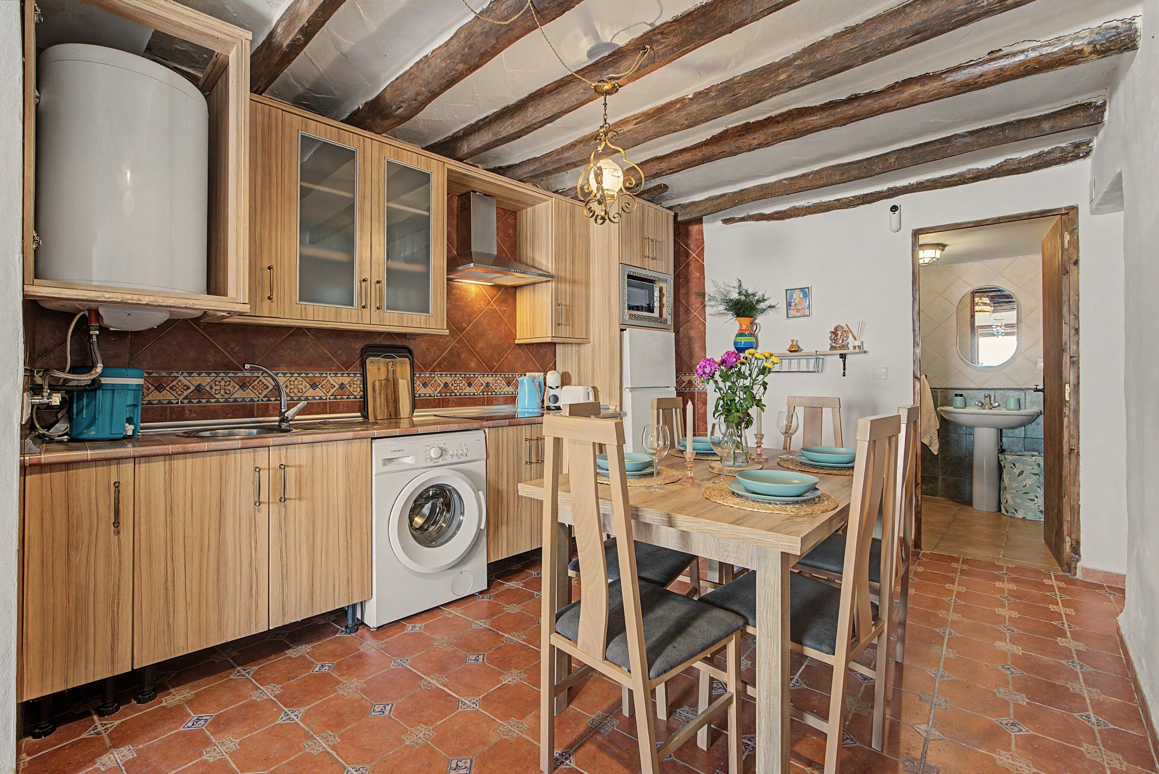 Une cuisine compacte avec des meubles en bois, un lave-linge et un coin repas avec une table dressée pour quatre personnes.