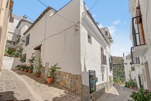 A narrow street with white buildings, stone walls, and potted plants.
