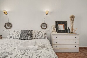 Un dormitorio con cama, cómoda, apliques de pared, espejo y objetos decorativos.
