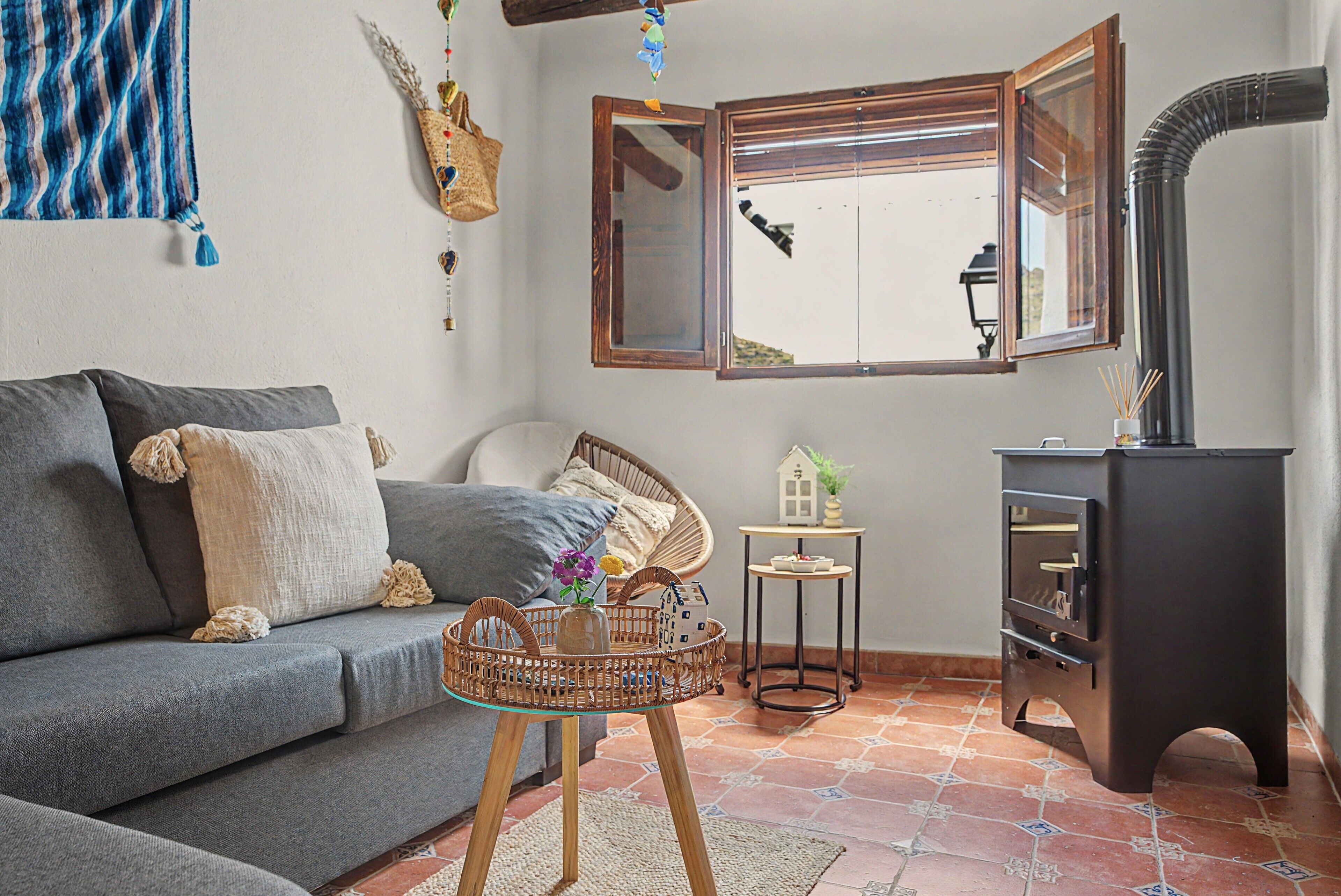 Una sala de estar acogedora con un sofá gris, un sillón de mimbre, una mesita con un modelo de casa y un mueble negro con espejo.