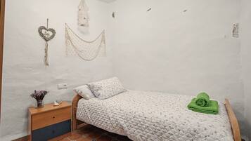 Un dormitorio pequeño y acogedor con una cama individual, una mesita de noche, una hamaca decorativa y un jarrón pequeño con flores.
