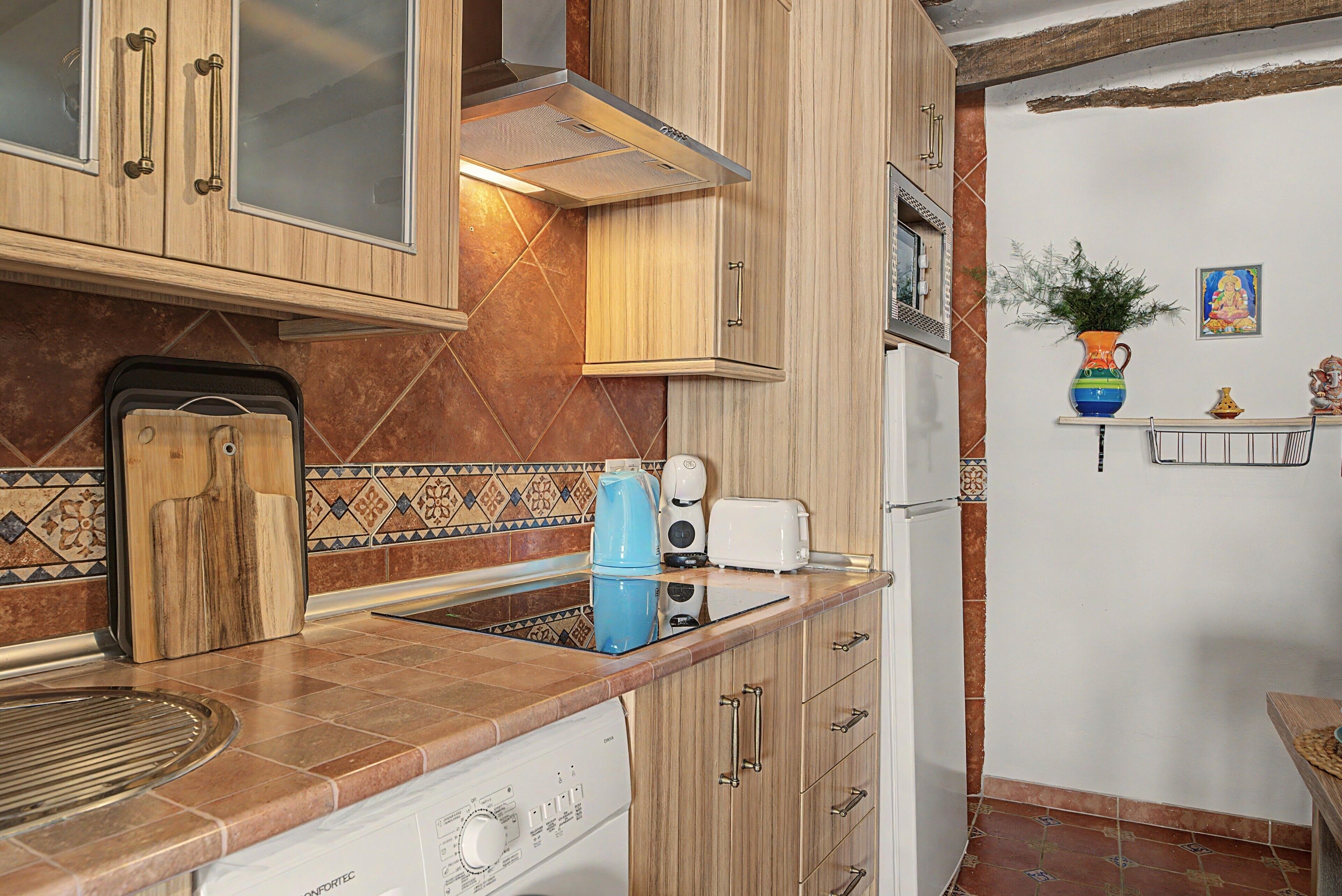 Eine Küche mit Holzausstattung, einer gefliesten Spritzschutzwand, einem Toaster, einem Wasserkocher und einem Spülbecken.