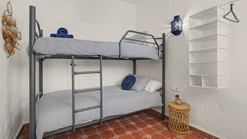 A bunk bed with striped bedding, a small round table with a vase, and a wall-mounted shelf with folded towels.