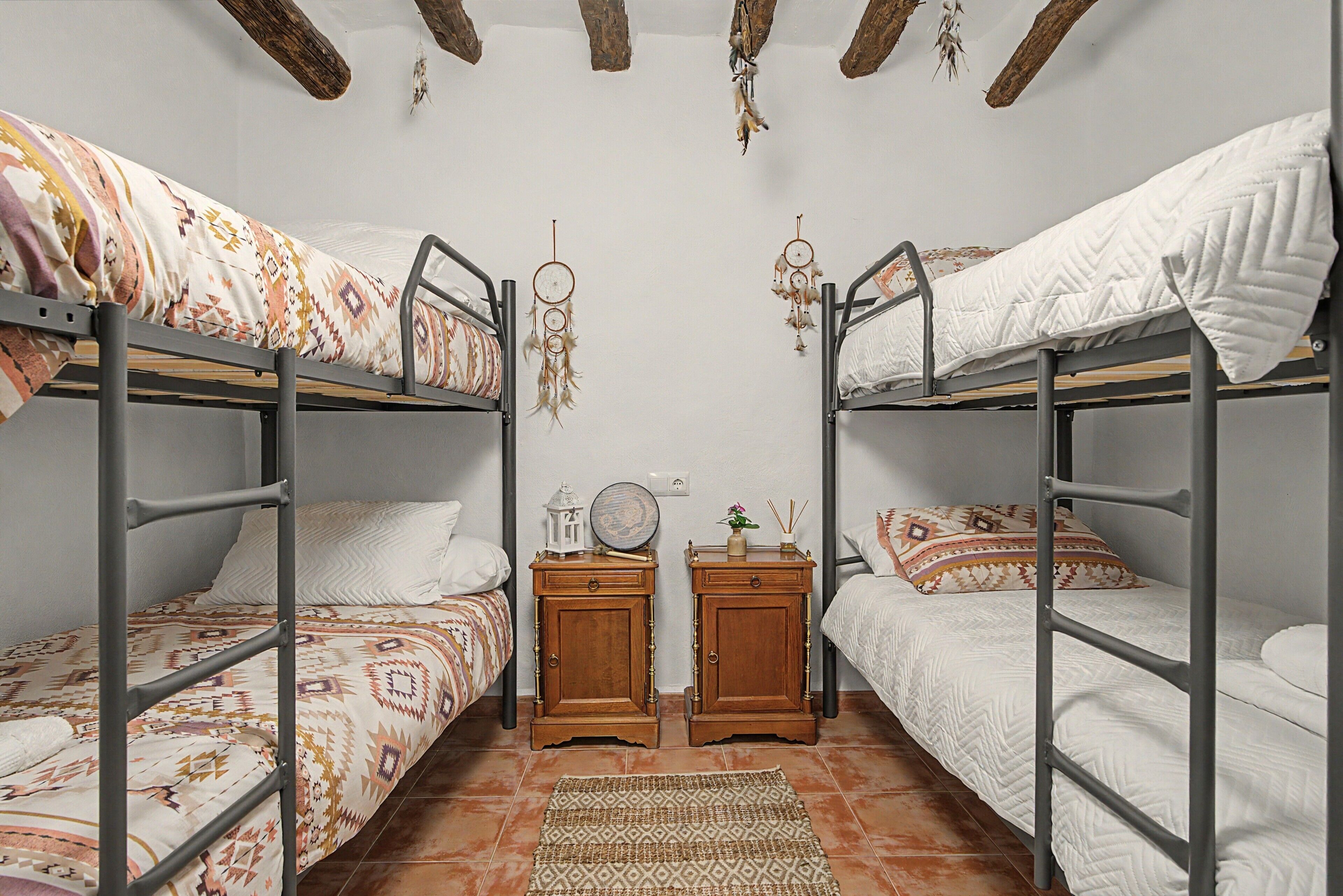 A dormitory room with bunk beds, a wooden nightstand, a dreamcatcher, and a small mirror.