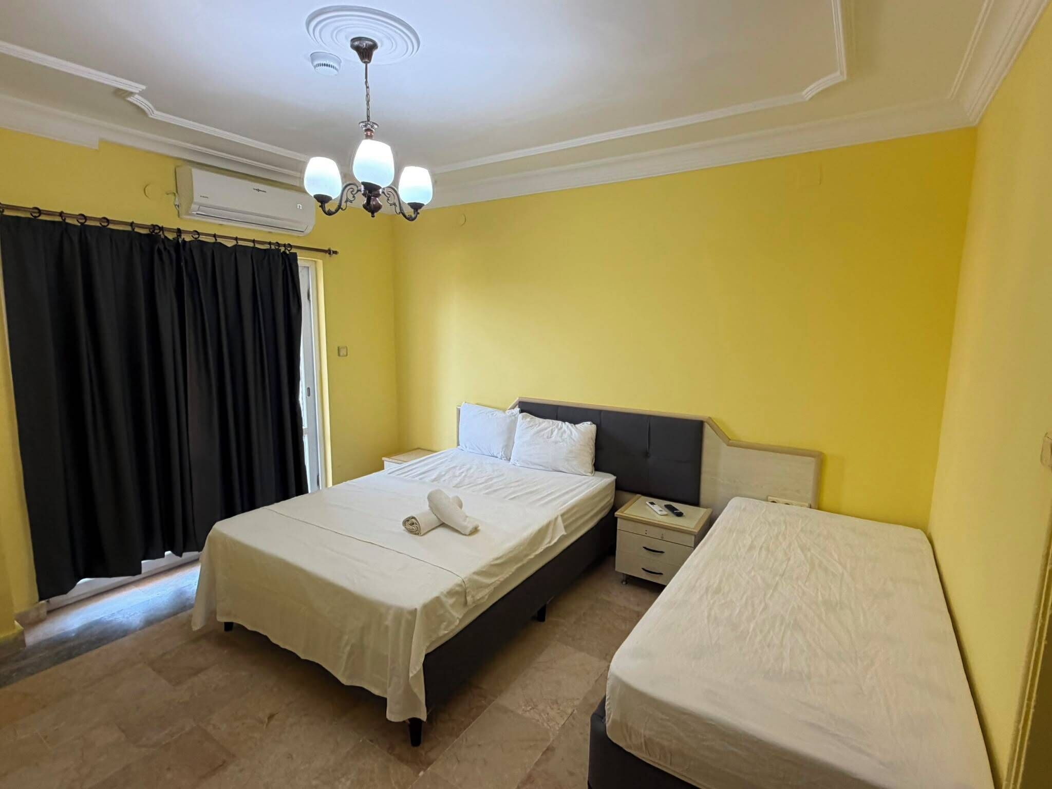 A hotel room with a bed, a nightstand, a bedside table, and a window with curtains.
