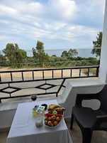 A balcony with a table set for a meal, a candle, and a view of the sea and greenery.